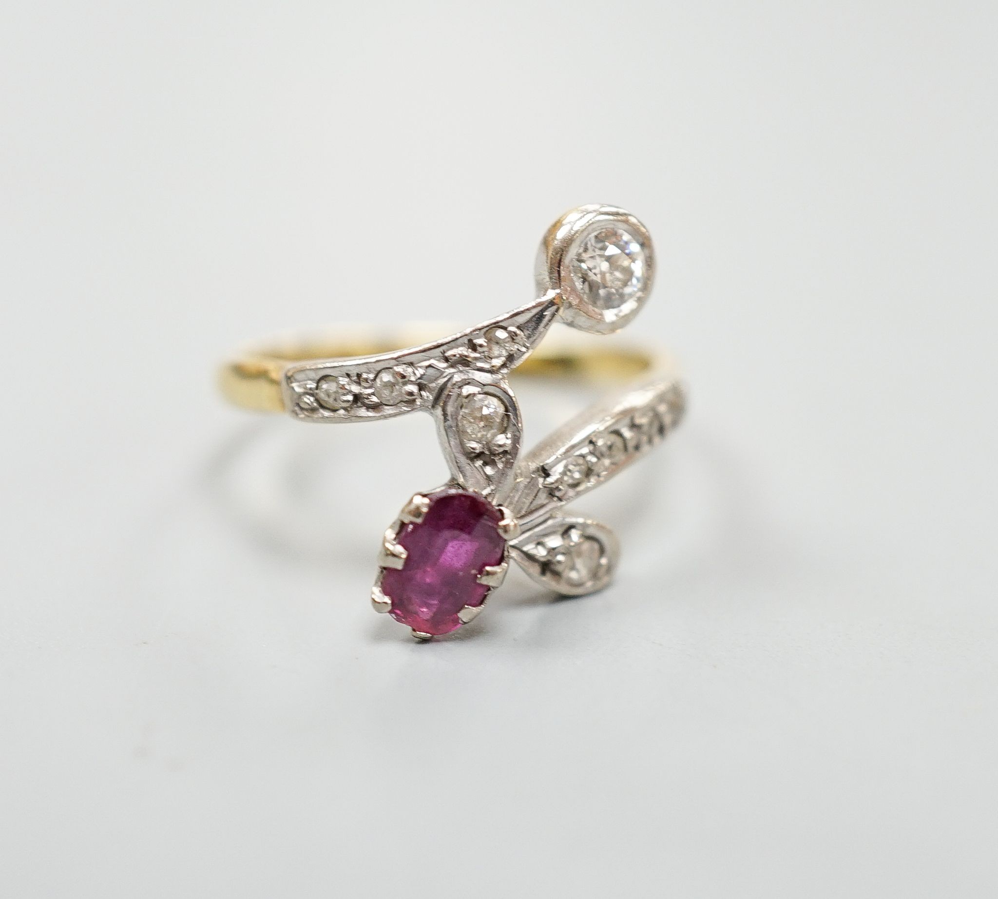 An early to mid 20th century 18ct, ruby and diamond set crossover ring, with diamond set shoulders, size Q/R, gross 4.7 grams.